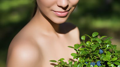 Woman holding fresh wild bilberries and green leaves outdoors, representing wild bilberry extract used in ORY Skincare for antioxidant and skin-brightening benefits.