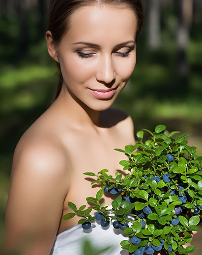 Woman holding fresh wild bilberries and green leaves outdoors, representing wild bilberry extract used in ORY Skincare for antioxidant and skin-brightening benefits.