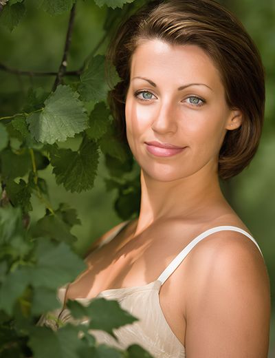 Woman with clear, balanced skin standing among green leaves, representing Witch Hazel Extract used in ORY Skincare for soothing, toning, and refining pores.