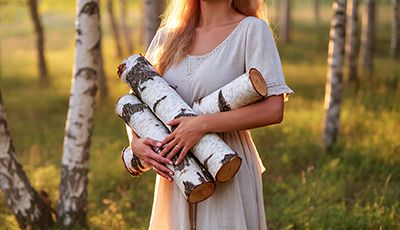 Woman holding birch logs in a sunlit forest — natural birch bark extract skincare ingredient for ORY Skincare.