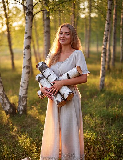 Woman holding birch logs in a sunlit forest — natural birch bark extract skincare ingredient for ORY Skincare.