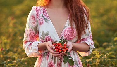 Woman holding fresh rosehips in a field, representing rosehip extract as a natural ORY Skincare ingredient rich in antioxidants and skin-nourishing nutrients.