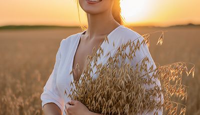 Woman in an oat field holding fresh oats at sunset — soothing colloidal oat skincare ingredient for ORY Skincare.