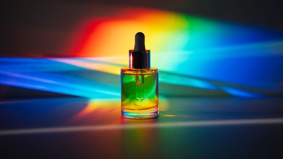 Glass serum bottle illuminated by a full color spectrum of light, symbolizing the emotional and psychological impact of color in skincare rituals.