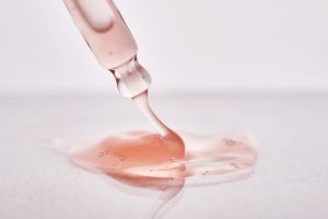 Close-up of a blush-toned skincare serum flowing from a glass dropper, showcasing texture, viscosity, and precision formulation.
